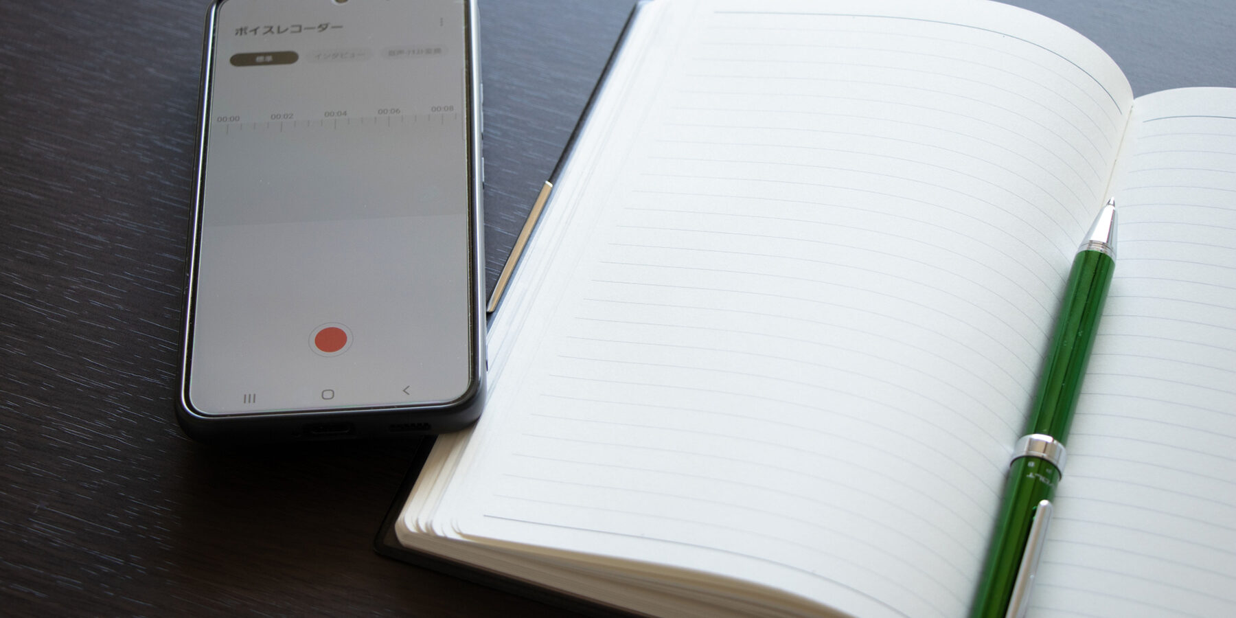 スマホのボイスレコーダーとノートとペンでインタビュー取材のイメージ写真