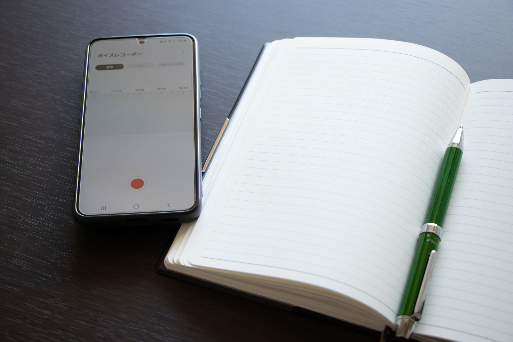 スマホのボイスレコーダーとノートとペンでインタビュー取材のイメージ写真